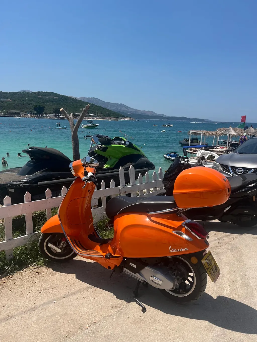 An orange Vespa parked by a turquoise beach