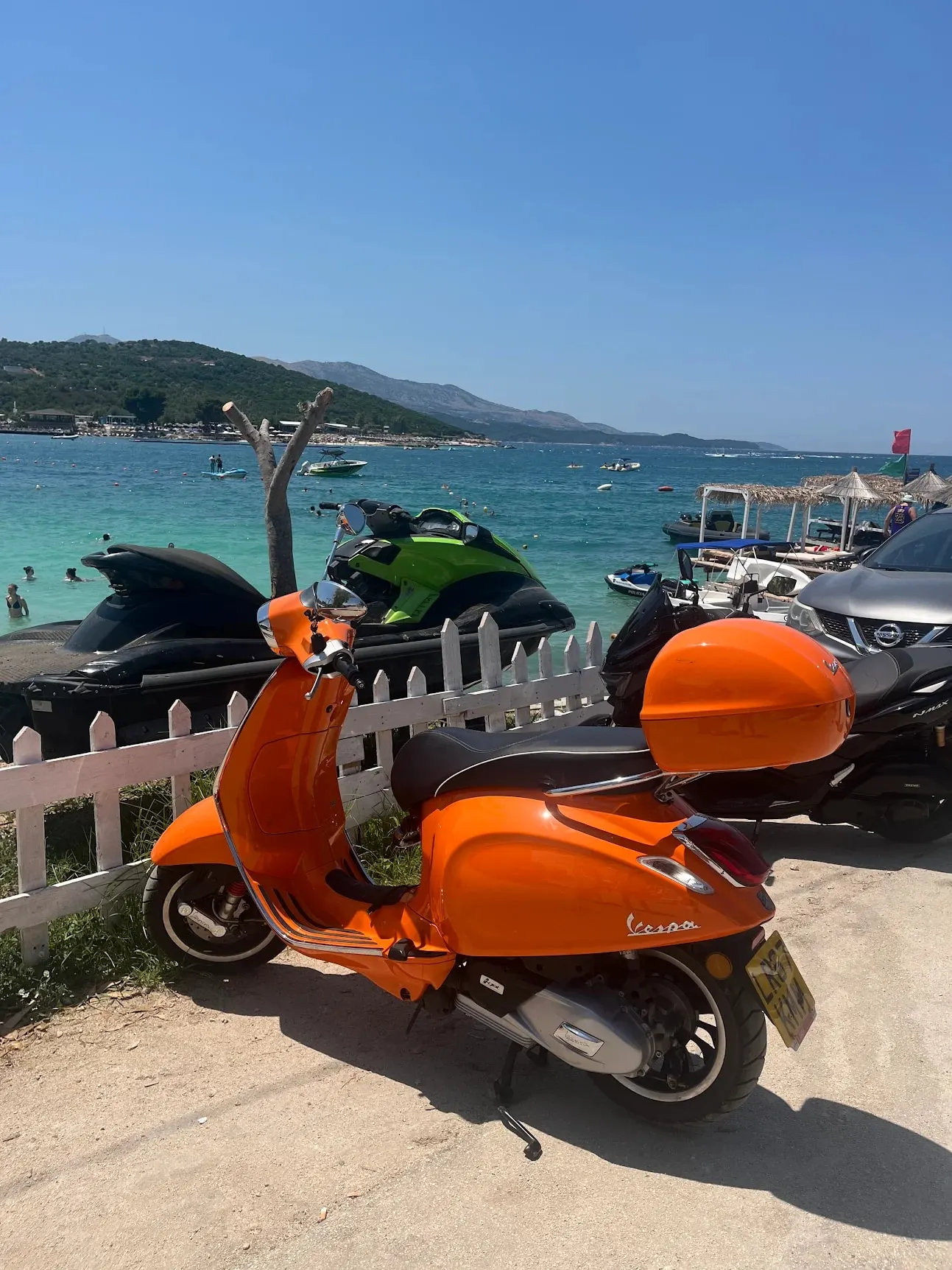 An orange Vespa parked by a turquoise beach