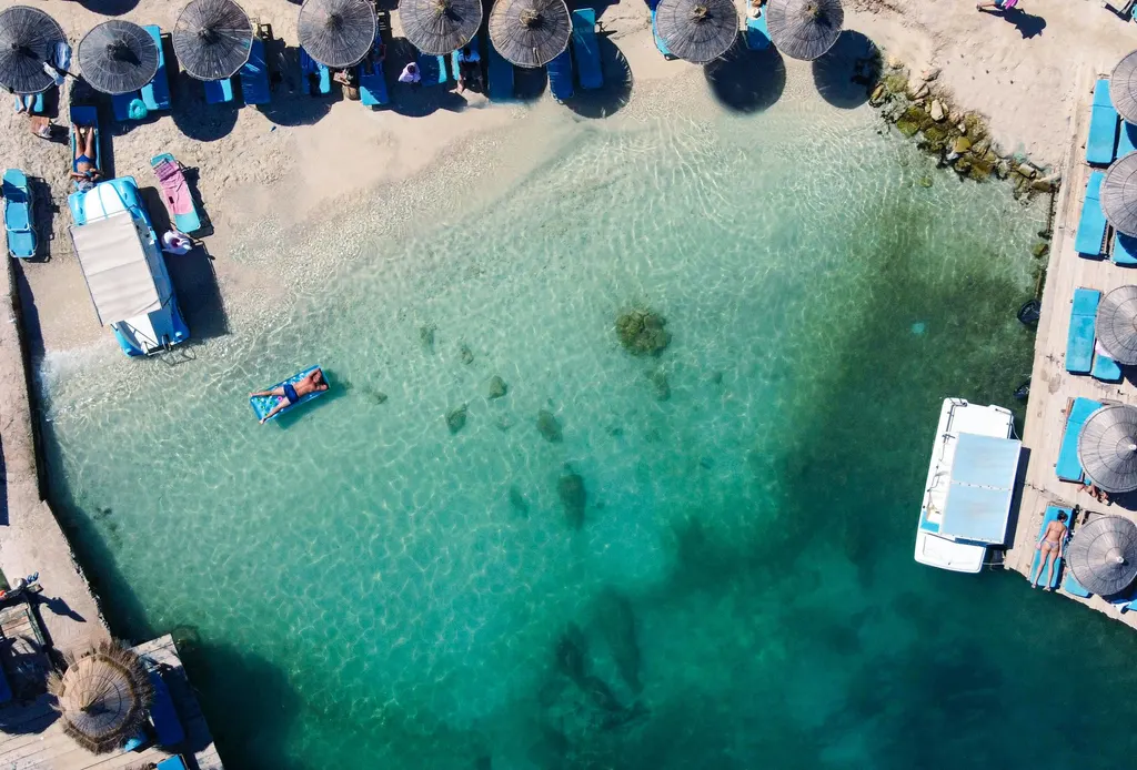 A beach from above, with clear turquoise water and straw umbrellas