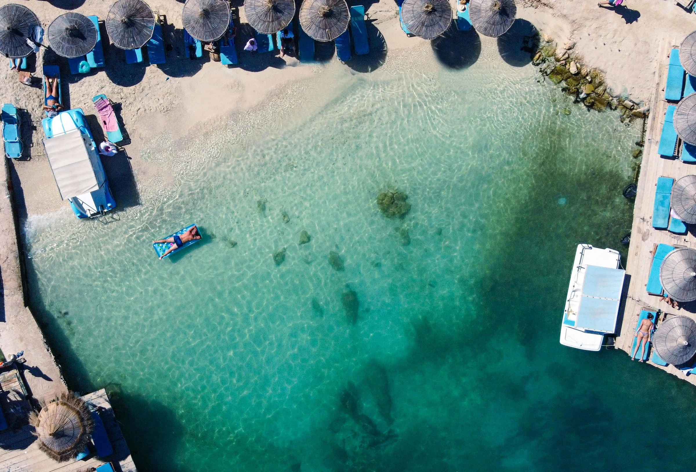 A beach from above, with clear turquoise water and straw umbrellas