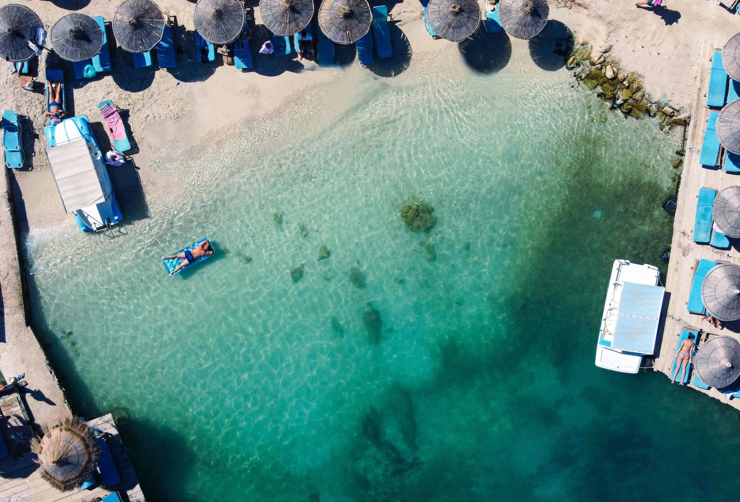 A beach from above, with clear turquoise water and straw umbrellas