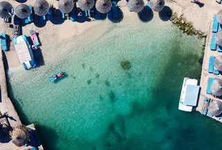 A beach from above, with clear turquoise water and straw umbrellas